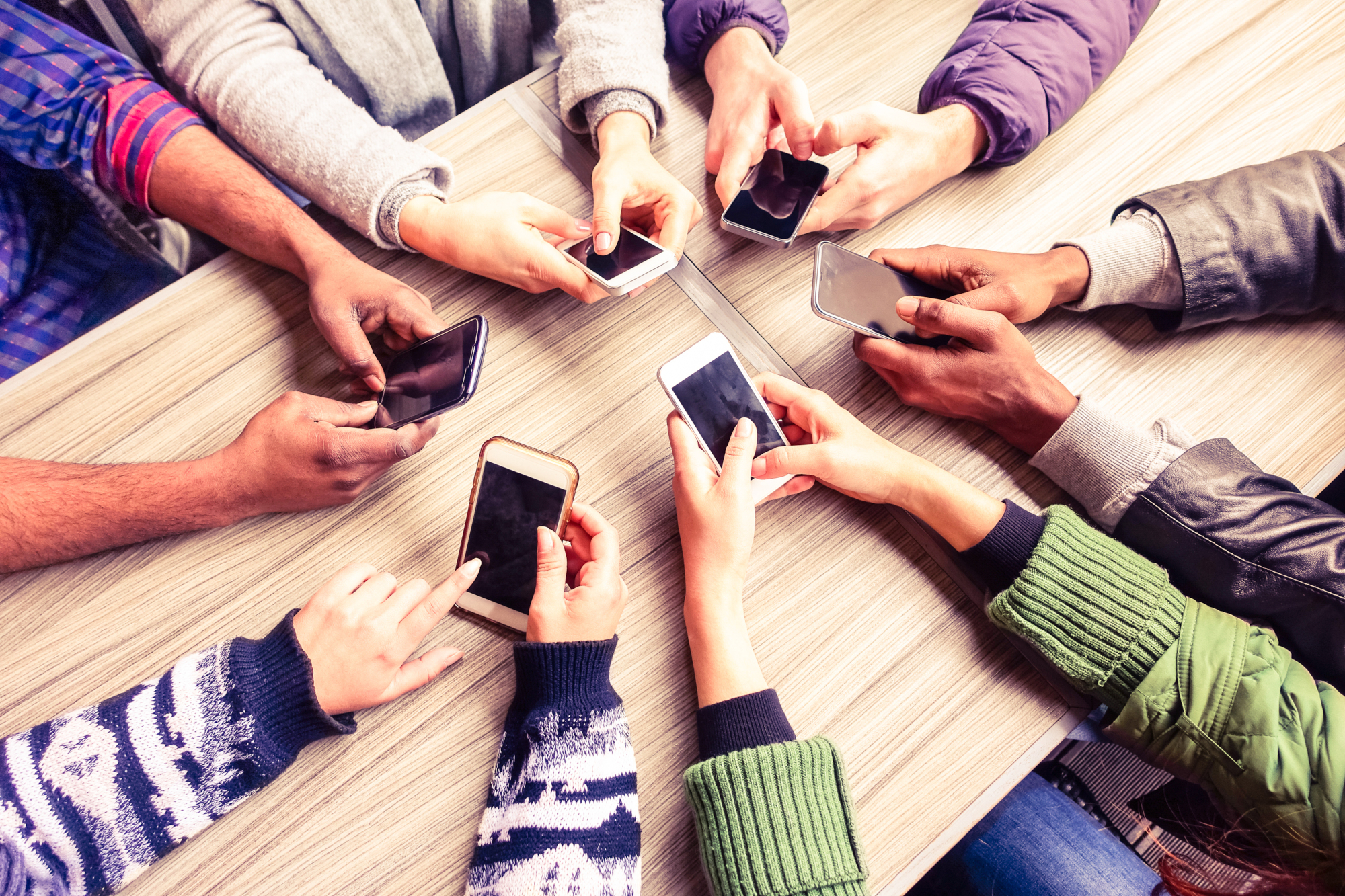 Six pairs of hands using mobile phones around a table